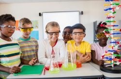 a number of children at a science lab table with colorful beakers and safety glasses